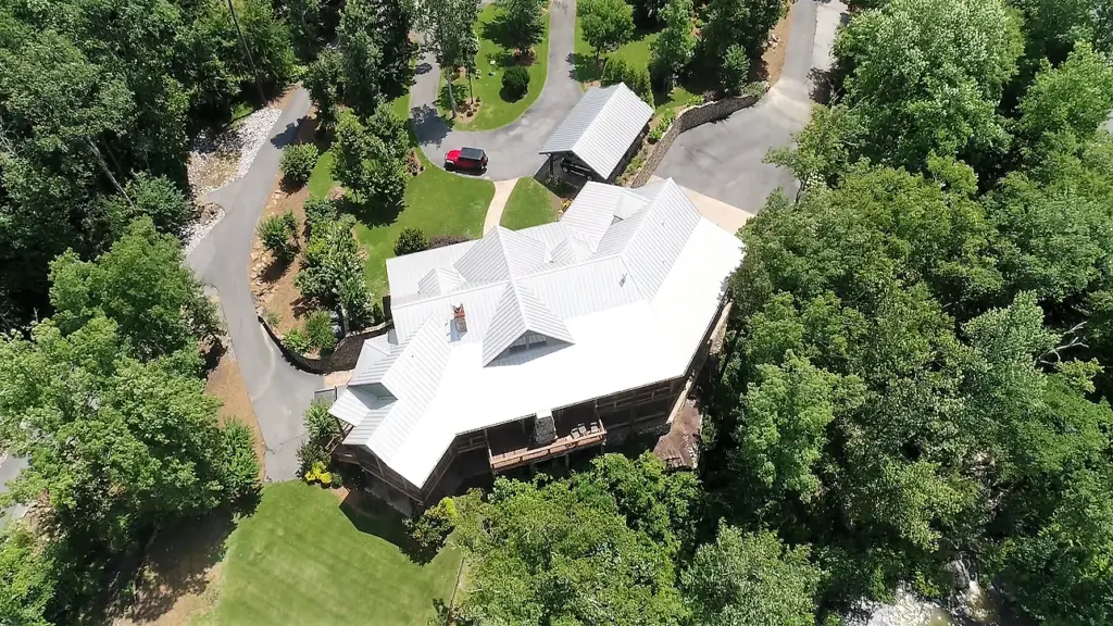 Aerial view of residential home with white metal roof with green trees surrounding