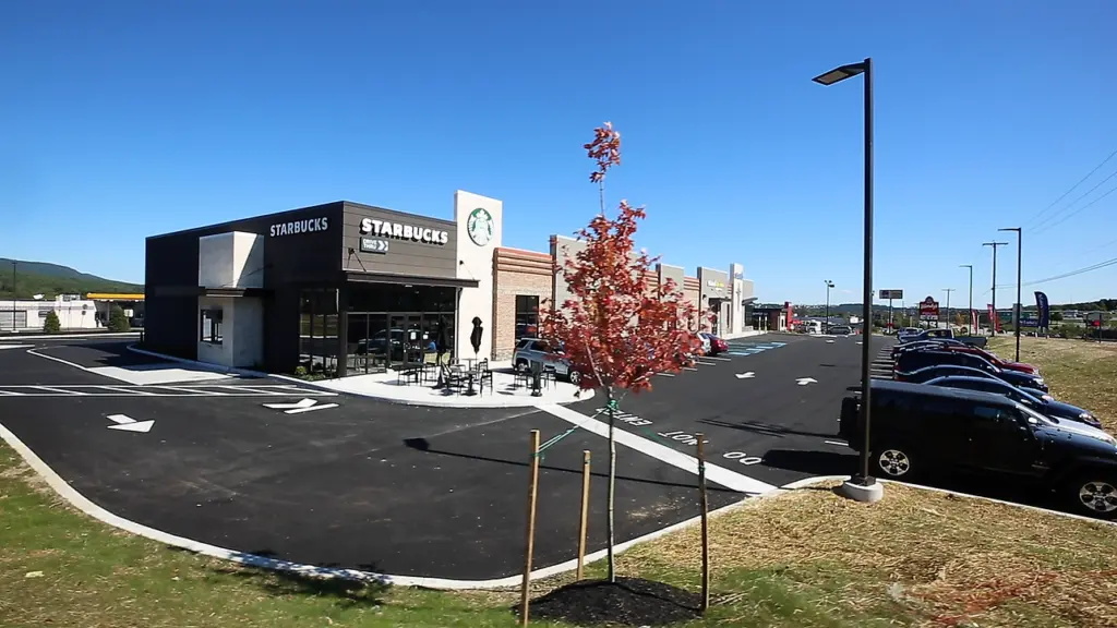 Exterior of Starbucks building with a dark asphalt parking lot and fall foliage